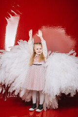 little girl 4 years old in white angel wings on a red latex background in the studio for valentine's day