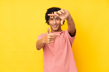 Young african american man isolated on yellow background focusing face. Framing symbol