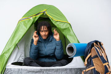 Young african american man inside a camping green tent with fingers crossing and wishing the best