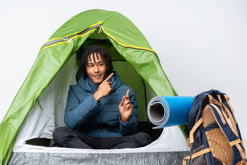 Young african american man inside a camping green tent frightened and pointing to the side