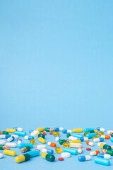 Vertical photo of many different pills and capsules on blue background. Photo with free empty space above colorful pills
