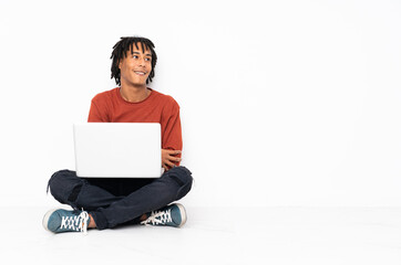 Young african american man sitting on the floor and working with his laptop happy and smiling