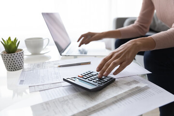 Close up young woman calculating monthly domestic utility bills using computer e-banking...