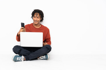 Young african american man sitting on the floor and working with his laptop making a selfie