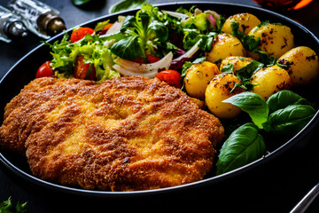 Breaded fried pork chop, French fries and vegetables on white background
