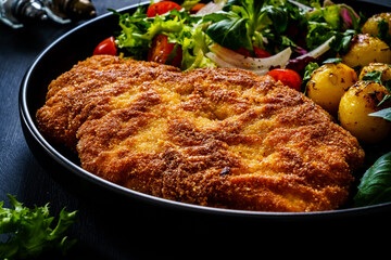 Breaded fried pork chop, French fries and vegetables on white background
