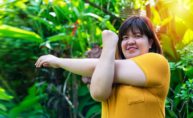 Healthy weight loss concept. Happy overweight young woman stretching before workout in the garden. Fat girl obesity stretch arm warm up before exercising in the morning at home.