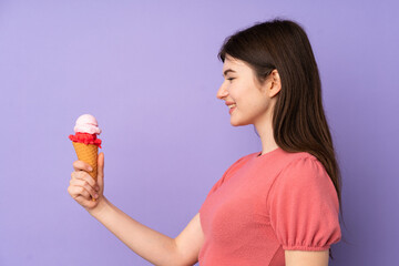 Young Ukrainian teenager girl holding a cornet ice cream over isolated purple background with happy expression