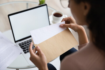 Close up young woman opening envelope with letter, feeling curious of getting news. Back rear view millennial lady receive postal mail with important document, invitation or bank notification.