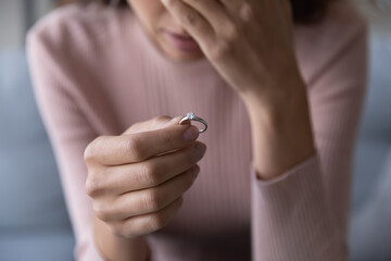 Close up frustrated millennial unhappy desperate woman holding engagement ring with diamond in hand, suffering from relations breakup or fiancee betrayal, denied marriage or getting divorced.