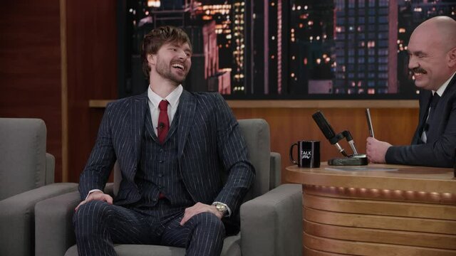 MED TO CU ZOOM IN Late-night talk show host having a funny conversation with celebrity male guest in a studio. TV broadcast style show. Shot with RED cinema camera