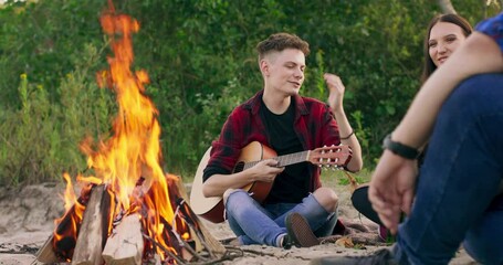 Close up view of young boy joking with their friends while having a picnic at the riverbank. Bright sunset, having leisure time. The teenager is going to play the guitar. - Powered by Adobe