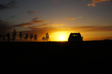 Mitternachtssonne in Island mit Auto und Bäume als schwarze Silhouette, Autoreisen in Island bei...