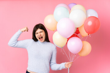 Young Ukrainian teenager girl holding lots of balloons over isolated pink background celebrating a victory