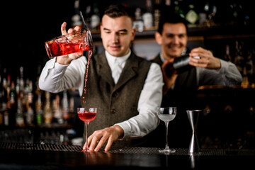 beautiful view of bartender man pouring cocktail from cup to glass on the bar counter.