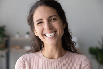 Head shot close up young pretty caucasian woman looking at camera, feeling happiness alone at home....