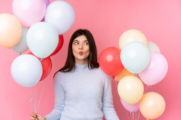 Young Ukrainian teenager girl holding lots of balloons over isolated pink background