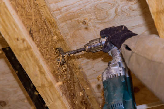 Construction work plumber drilling hole in joist for sewage pipeline preparing hole for plumbing drain