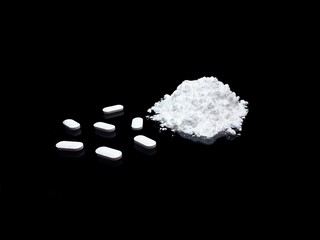 Cocaine drug powder and pills on black background