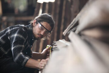 Carpenter, joiner is working in the workshop. Man at work on wood.Image of mature carpenter in the workshop,furniture making concept. - obrazy, fototapety, plakaty