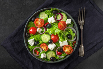 Greek salad. Vegetable salad from fresh vegetables, feta cheese and olives in a plate over towel with fork on black table