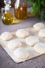 fluffy pizza dough lies on a wooden board on a dark table next to olive oil and herbs. making homemade pizza.
