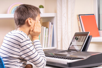 Teenage boy watching video lesson at tablet computer and learing playing digital piano at home. Online learning remote education