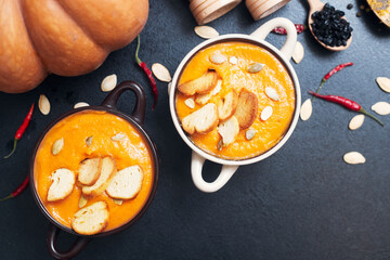 pumpkin cream soup with croutons on a black table with spices