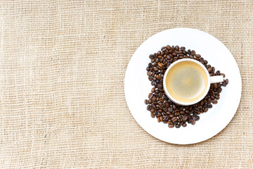 Heart symbol made of roasted coffee beans and a coffee cup on a burlap cloth background