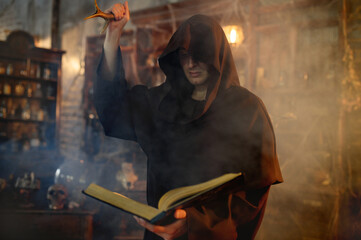 Male exorcist in black hood holds book of spells