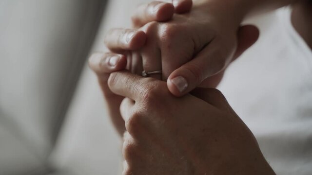 Close-up, caucasian hands of man and woman touching, hugging tightly. On woman hand there is engagement ring