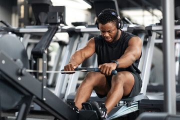 Fototapeta na wymiar Motivated black sportsman having workout on rowing machine