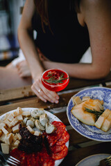 
a girl in a black T-shirt sits at a table and holds a cocktail in her hands at sunset. cheese and meat platter. cut melon