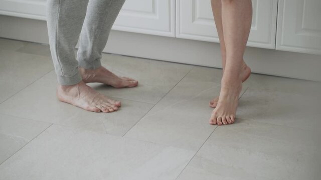 Close-up of caucasian woman bare feet are spinning near male feet on tile, approaching him
