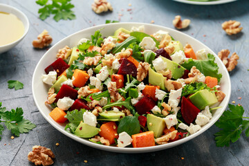 Healthy Butternut squash salad with beetroot, avocado, walnut and feta cheese in white bowl