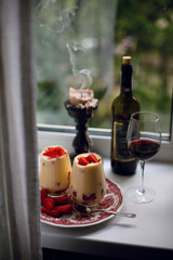 dessert with fresh raw strawberries and a glass of red wine near the window. red wine bottle. tiramisu with strawberries. candle near window