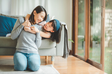 Happy Asian mother and cute little daughter having fun while playing and hugging at home in living room - Powered by Adobe