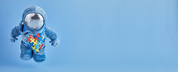 World Autism awareness day background. Blue plush astronaut toy with puzzle heart, autism symbol, on blue background