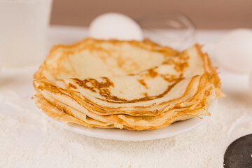 beautiful round thin pancakes on the kitchen table with flour and whisk and eggs