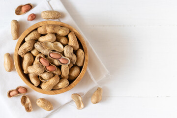Top view of peanuts in a wooden bowl on white background,