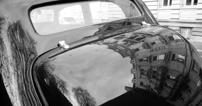Black and white 4K DCI footage of rear view over retro old vintage car with typical Haussmannian building reflected in the shiny paint of the car