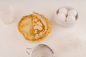 thin round pancakes with chicken eggs and flour on a white plate fried