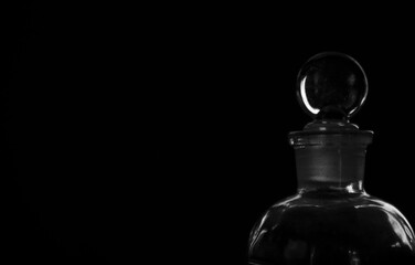 Antique glass vial with round stopper on black background with sharp, bright highlights and negative space for copy