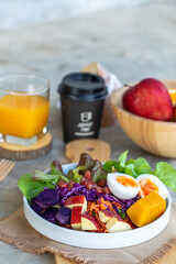 Healthy salad of fresh vegetables - egg, carrot, purple cabbage, pumpkin, apple, purple sweet potato and pomegranate on a bowl with orange juice and coffee. Healthy breakfast.