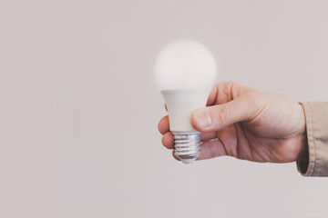 Man hand holding illuminated light bulb against beige background