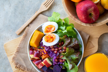 Healthy salad of fresh vegetables - egg, carrot, purple cabbage, pumpkin, apple, purple sweet potato and pomegranate on a bowl with orange juice. Healthy breakfast. Flat lay. Top view.