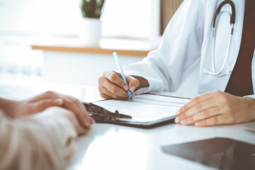 Unknown woman-doctor filling up an application form while consulting patient. Medicine concept