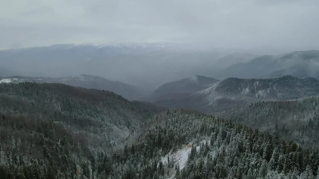 Flying over mountains in winter time with bad weaather. Birds eye view over the mountain range.