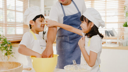 Happy smiling young Asian Japanese family with preschool kids have fun play and laugh while cook cake for breakfast meal in modern kitchen home in morning. Doing bakery knead dough and bake cookies.
