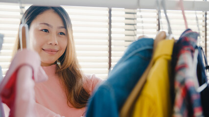 Beautiful attractive young Asia lady choosing her fashion outfit clothes in closet at house or store. Girl think what to wear casual shirt. Home wardrobe or clothing shop changing room.